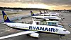 Flera Ryanair-plan parkerade på en flygplats med soluppgång och terminaler i bakgrunden.