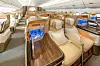 Emiratesin Business Class -matkustamo, jossa on vaaleita istuimia, puupintaisia pöytiä ja viihdenäyttöjä.