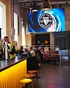 Asiakkaita istuu Guinness Open Gate Brewery -panimoravintolassa baaritiskin ja ison logonäytön alla.