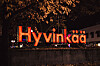 Valaistu Hyvinkää-kyltti syksyisessä kaupunkimaisemassa iltahämärässä.