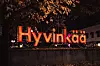 Valaistu Hyvinkää-kyltti syksyisessä kaupunkimaisemassa iltahämärässä.