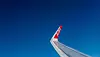 AirAsia-flygplans vinge med röd logotyp mot klarblå himmel.