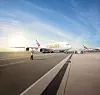 Ett Emirates-flygplan står parkerat på en flygplatsplatta i kvällsljus med markpersonal i förgrunden.