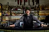 Mies seisoo hotellibaarin tiskin takana pullohyllyjen edessä.