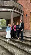 Neljä ihmistä seisoo portaitten yläosassa punatiilisen rakennuksen sisäänkäynnin edessä.