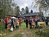 Ihmisiä seisoo nurmikolla punaisiksi maalattujen puutalojen ja pöytien äärellä museopihalla.