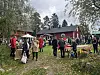 Ihmisiä seisoo nurmikolla punaisiksi maalattujen puutalojen ja pöytien äärellä museopihalla.