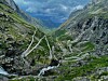 Snoet vej gennem en grøn fjelddal omgivet af stejle klipper og bjerge.