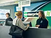 To personer står ved en Enterprise Rent-A-Car-skranke i en lufthavn med en medarbejder bag disken.