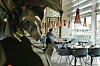 En ljus restaurang med dukade bord, blå stolar, stora fönster och hängande lampor.