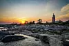 Kivinen rantakallio, matala vesi ja majakka auringonlaskussa.