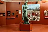 Museosalissa seisoo vihertävä Havis Amanda -veistos jalustalla kaupungin historiasta kertovan seinäkuvan edessä.