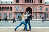 Två personer dansar på en stenlagd gata framför en rosa byggnad med valv, fönster och balkonger.