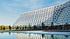 Stort terrasserat hotell som reflekteras i lugnt vatten vid en blå himmel.