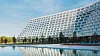 Stort terrasserat hotell som reflekteras i lugnt vatten vid en blå himmel.