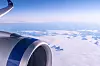 Vy från ett flygplansfönster med en stor jetmotor och blå himmel ovanför vita moln.