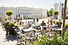 Aurinkoinen sisäpiha, jossa on pöytiä, kukkia ja taustalla historiallisia rakennuksia.