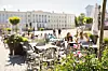 Aurinkoinen sisäpiha, jossa on pöytiä, kukkia ja taustalla historiallisia rakennuksia.