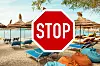 Röd STOPP-skylt framför solstolar, parasoller och säckstolar på en strand.