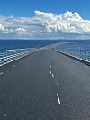 Pitkä silta kulkee merimaiseman yli kohti horisonttia pilvisen taivaan alla.