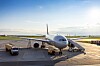 Passagerarflygplan parkerat på flygplatsens ramp med ett fordon bredvid.