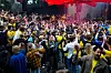 Stor folkmassa dansar och jublar i en lokal med röd belysning.