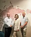 Kolme henkilöä seisoo karttaseinän edessä sisätiloissa.