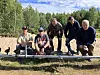 Viisi miestä poseeraa ulkona ampumaradalla pitkän metallisen telineen vieressä metsäisessä ympäristössä.