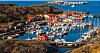 Småbåtshamn med röda sjöbodar, bryggor och många båtar vid klippig kust någonstans på svenska västkusten.