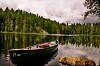 Punainen kanootti ja kivi tyynen järven rannalla, taustalla tiheä havumetsä.