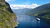 Två fartyg seglar i en smal fjord i Flåm i Norge mellan höga berg och grönklädda sluttningar.