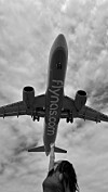 Mustavalkoinen näkymä lentokoneen vatsapuolelta taivaalla, Flynas-logo näkyy rungossa.