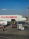 Air Arabian matkustajakone ja maahuoltoajoneuvoja lentokentän asematasolla sinisen taivaan alla.