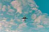 Passagerarflygplan sett underifrån mot en blå himmel med vita moln.