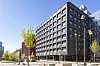 Hög mörk hotellbyggnad vid ett torg i centrala Stockholm, omgiven av träd, gator och gångtrafikanter.