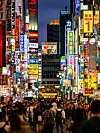 Ihmisjoukko vilkkaalla Tokion Shinjukun kadulla kirkkaiden japanilaisten mainoskylttien ympäröimänä.