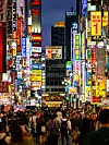 Ihmisjoukko vilkkaalla Tokion Shinjukun kadulla kirkkaiden japanilaisten mainoskylttien ympäröimänä.