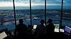 Silhuetter av flygledare vid datorskärmar med utsikt över en flygplats.