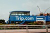 Sininen Trip.com-kaksikerroksinen bussi kukkaistutusten takana.