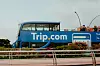 Sininen Trip.com-kaksikerroksinen bussi kukkaistutusten takana.