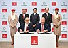 Kuusi henkilöä allekirjoittaa sopimusta pöydän ääressä Emirates-logojen edessä.