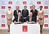 Kuusi henkilöä allekirjoittaa sopimusta pöydän ääressä Emirates-logojen edessä.