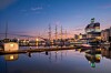Gothenburg harbour at dusk, with boats, cranes and illuminated buildings reflected in calm water.