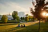 Ihmisiä nurmikolla puistossa ilta-auringon ja kaupunkimaiseman edessä.