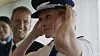 Naval officer adjusting a peaked cap as colleagues smile behind him.