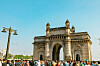 Väkijoukko Gateway of India -monumentin edustalla kirkkaan sinisen taivaan alla.