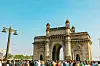 Väkijoukko Gateway of India -monumentin edustalla kirkkaan sinisen taivaan alla.
