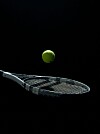 Vihreä tennispallo leijuu tennismailan yllä mustaa taustaa vasten.