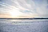 Auringonlasku jäätyneen vesistön yllä ja pieni vene horisontissa.