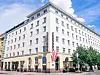 Vaalea koristeellinen hotellirakennus kadunkulmassa sinisen taivaan alla.
